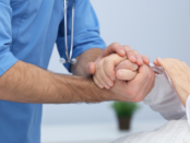 Doctor gently holding a patient's hand to provide comfort during a consultation.