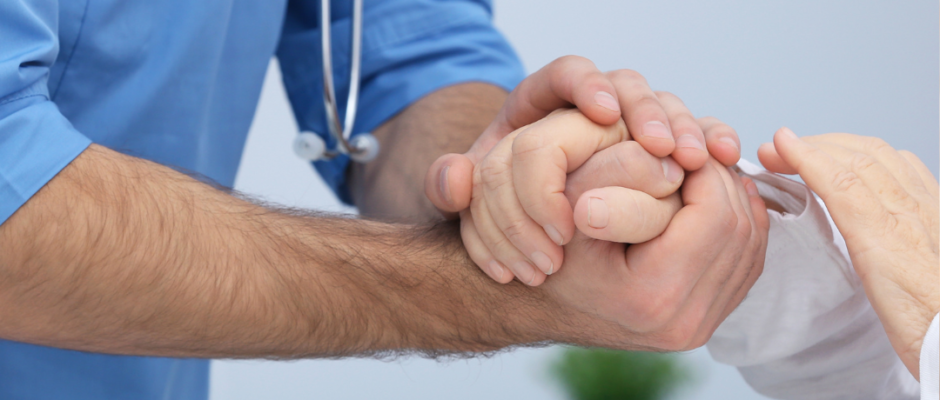 Doctor gently holding a patient's hand to provide comfort during a consultation.