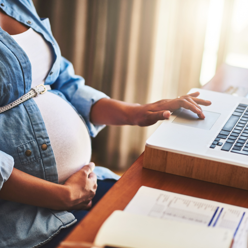 Pregnant working woman sitting at an ergonomic desk with a laptop, maintaining proper posture.