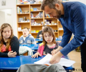 A diverse group of students in a classroom, with a teacher providing individualized support to a child with autism.